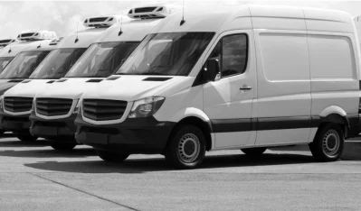 Fila de furgonetas blancas de carrocería alta aparcadas en un patio, vistas de frente