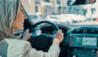 Mujer de pelo gris conduciendo y mirando la carretera, vista desde el asiento del copiloto