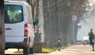 Furgoneta blanca aparcada en una calle arbolada con una mujer caminando al fondo entre la niebla