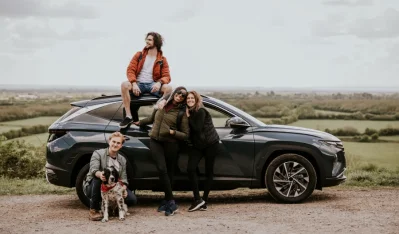 Familia con perro sentada sobre el techo de un SUV gris en un campo abierto