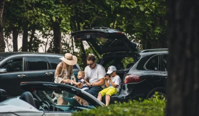 Familia sentada en el maletero abierto de un coche junto a un parque con árboles