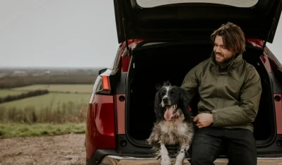 Hombre con perro en el maletero abierto de un SUV rojo en un campo