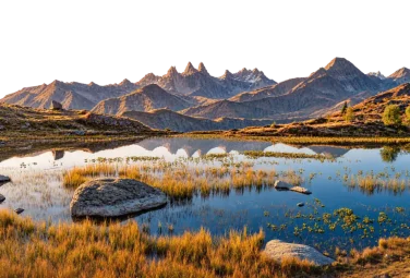 Lago de alta montaña con hierba dorada en las orillas y picos recortados al fondo