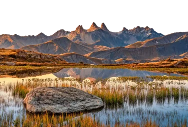 Lago de montaña con hierba alta y una gran roca junto a la orilla al amanecer