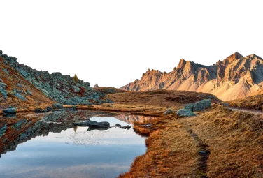 Laguna de montaña que refleja las laderas rocosas y los picos dorados al atardecer
