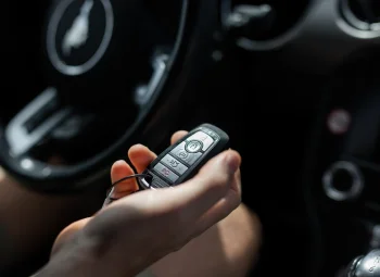 Mando de llave de coche en la mano junto al salpicadero de un vehículo oscuro