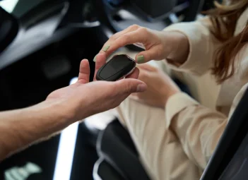 Entrega de un mando de llave dentro del habitáculo de un coche a una mujer de chaqueta beige