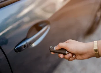 Mano abriendo con el mando la puerta de un coche de carrocería marrón