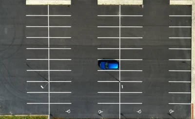 Vista aérea de un aparcamiento vacío con líneas blancas y un coche azul en una plaza