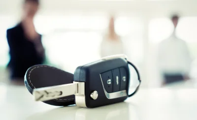 Llave de coche con mando sobre una mesa clara, con personas desenfocadas al fondo