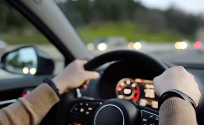 Manos al volante de un coche en una autovía con luces de tráfico desenfocadas