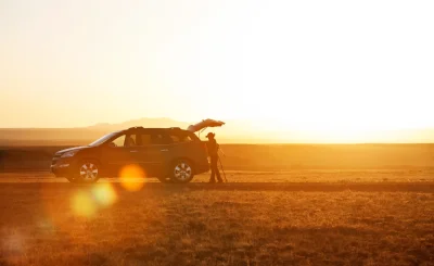 Coche con el maletero abierto en un campo dorado al atardecer, con destellos de sol