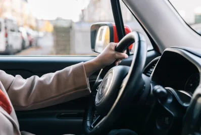 Mano con manga rosa sobre el volante de un coche, con una calle urbana desenfocada