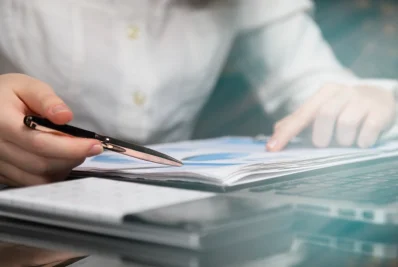 Manos firmando un contrato con bolígrafo sobre unos papeles en una mesa