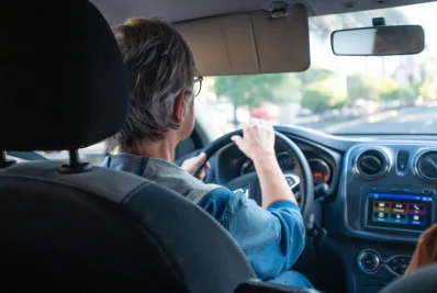 Mujer al volante vista desde el asiento trasero, con el salpicadero y la pantalla central