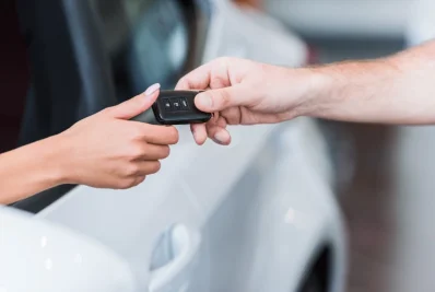 Entrega de llaves de coche con mando a distancia junto a un vehículo blanco