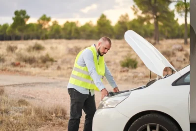 Mecánico con chaleco amarillo revisando el motor de un coche blanco con el capó abierto en un campo