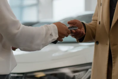 Mano que entrega un mando de llave de coche a otra mano junto a un vehículo blanco