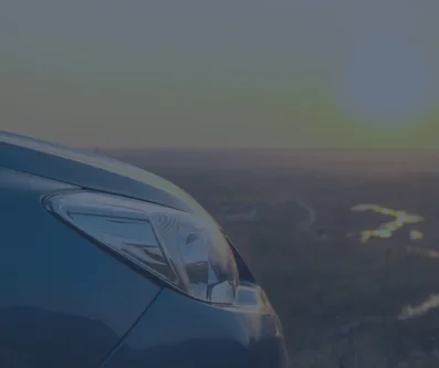 Detalle del faro de un coche con el cielo del atardecer reflejado en la carrocería