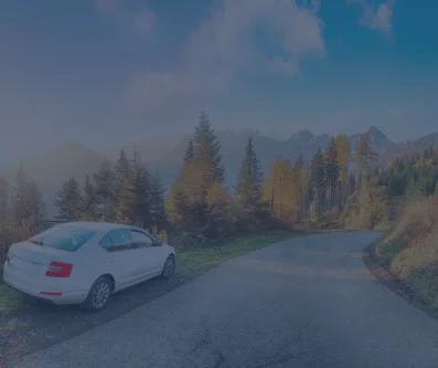 Coche blanco por una carretera de montaña entre bosque de otoño y picos al fondo