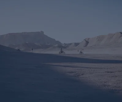 Llanura árida y montañas bajo un cielo gris oscuro con un sendero de tierra