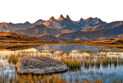 Lago de montaña con hierba alta y una gran roca junto a la orilla al amanecer