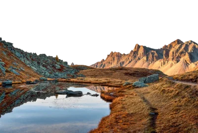 Laguna de montaña que refleja las laderas rocosas y los picos dorados al atardecer