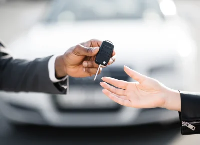 Hombre de traje entregando un mando de llave de coche frente a un vehículo blanco desenfocado