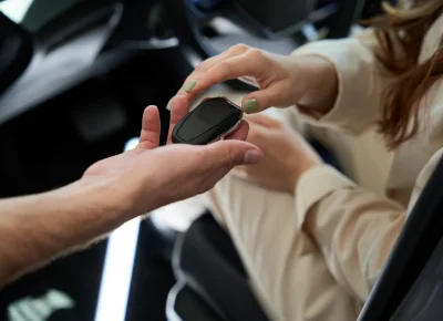 Entrega de un mando de llave dentro del habitáculo de un coche a una mujer de chaqueta beige