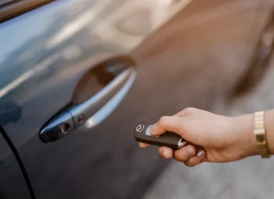Mano abriendo con el mando la puerta de un coche de carrocería marrón
