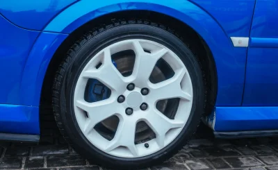 Rueda de aleación blanca de cinco radios en el paso de rueda de un coche azul brillante