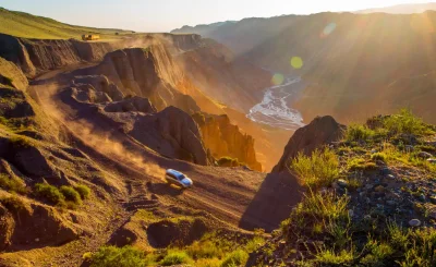 Cantera de roca rojiza con un coche diminuto en la pista del fondo y sol de frente