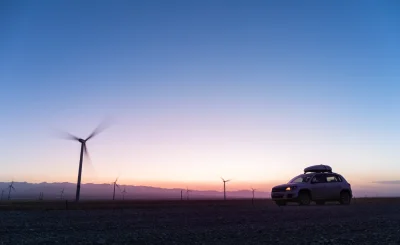 Coche con baca en un paisaje de aerogeneradores al atardecer