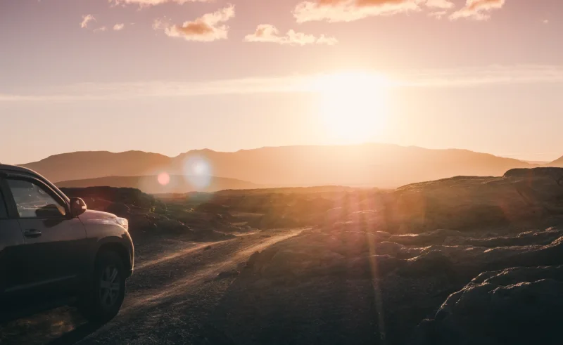 Silueta de un coche en una carretera de montaña con el sol al fondo y destellos de lente