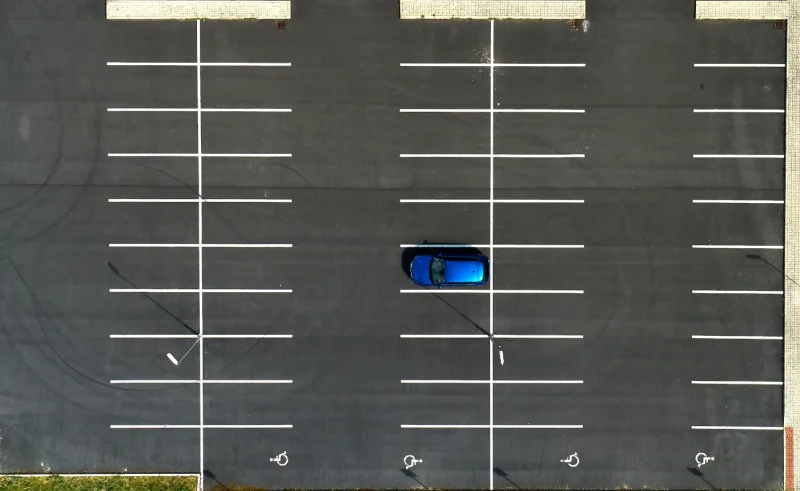 Vista aérea de un aparcamiento vacío con líneas blancas y un coche azul en una plaza