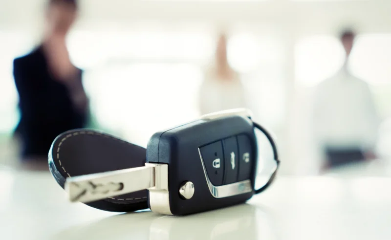 Llave de coche con mando sobre una mesa clara, con personas desenfocadas al fondo