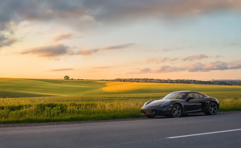 Coche deportivo negro circulando por una carretera recta entre campos al atardecer