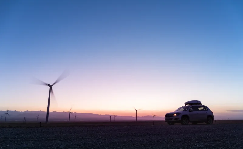 Coche con baca en un paisaje de aerogeneradores al atardecer