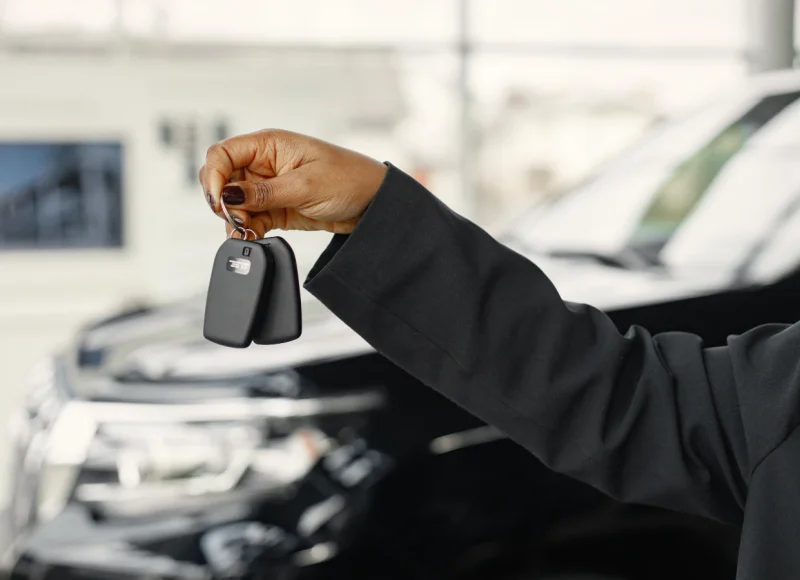 Mano de un hombre con traje sosteniendo unas llaves de coche junto a vehículos desenfocados