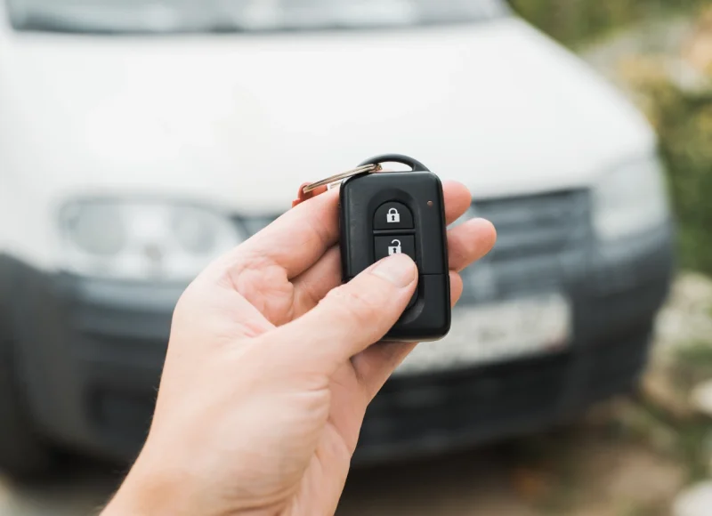 Mano sujetando una llave de coche con un vehículo blanco desenfocado detrás