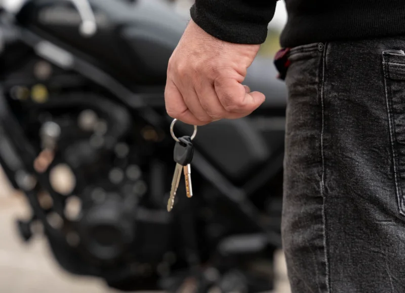 Hombre con vaqueros sujetando unas llaves junto a una moto negra desenfocada